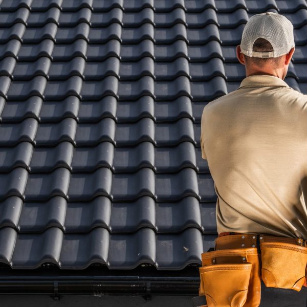 Professional Caucasian Roofing Contractor Worker Moving a Black Roof Ceramic Tiles in His Hands